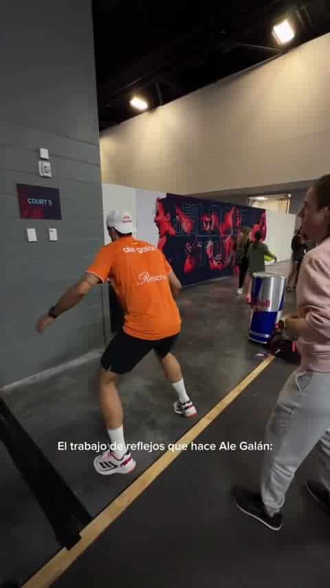 Athlete in an orange shirt and white cap sprinting down a hallway at a sports complex; a Court 5 sign is on the wall.